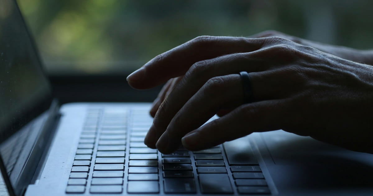 Hand typing on a laptop keyboard in backlight, next to a window