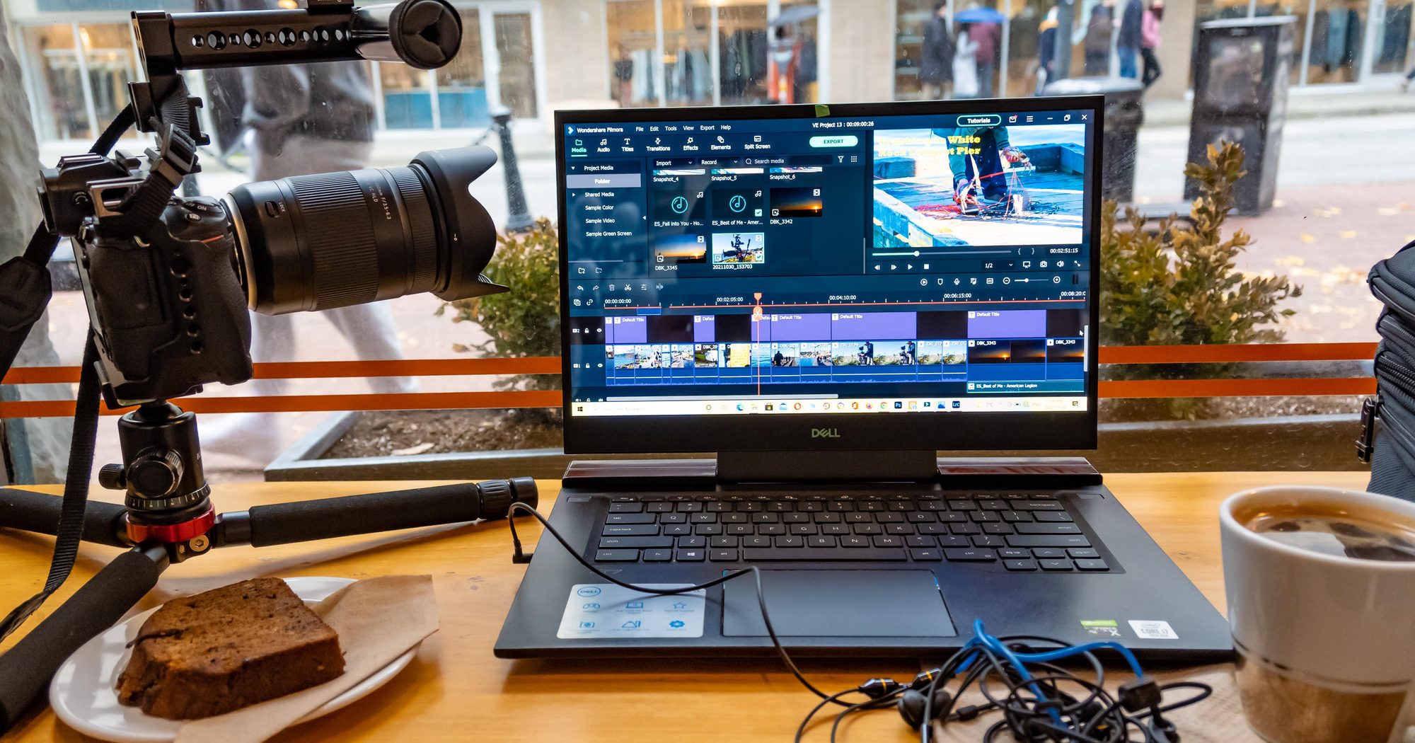 Camera on a tripod next to a laptop with a video editing timeline open, in a café